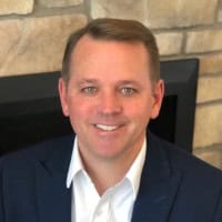 A man in a suit and white shirt is smiling in front of a stone wall, reflecting on his successful retirement planning for veterans.
